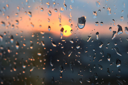 Regentropfen auf der Fensterscheibe; im Hintergrund taucht bei verhangenem Himmel die Sonne auf Regentropfen auf der Fensterscheibe; im Hintergrund taucht bei verhangenem Himmel die Sonne auf.